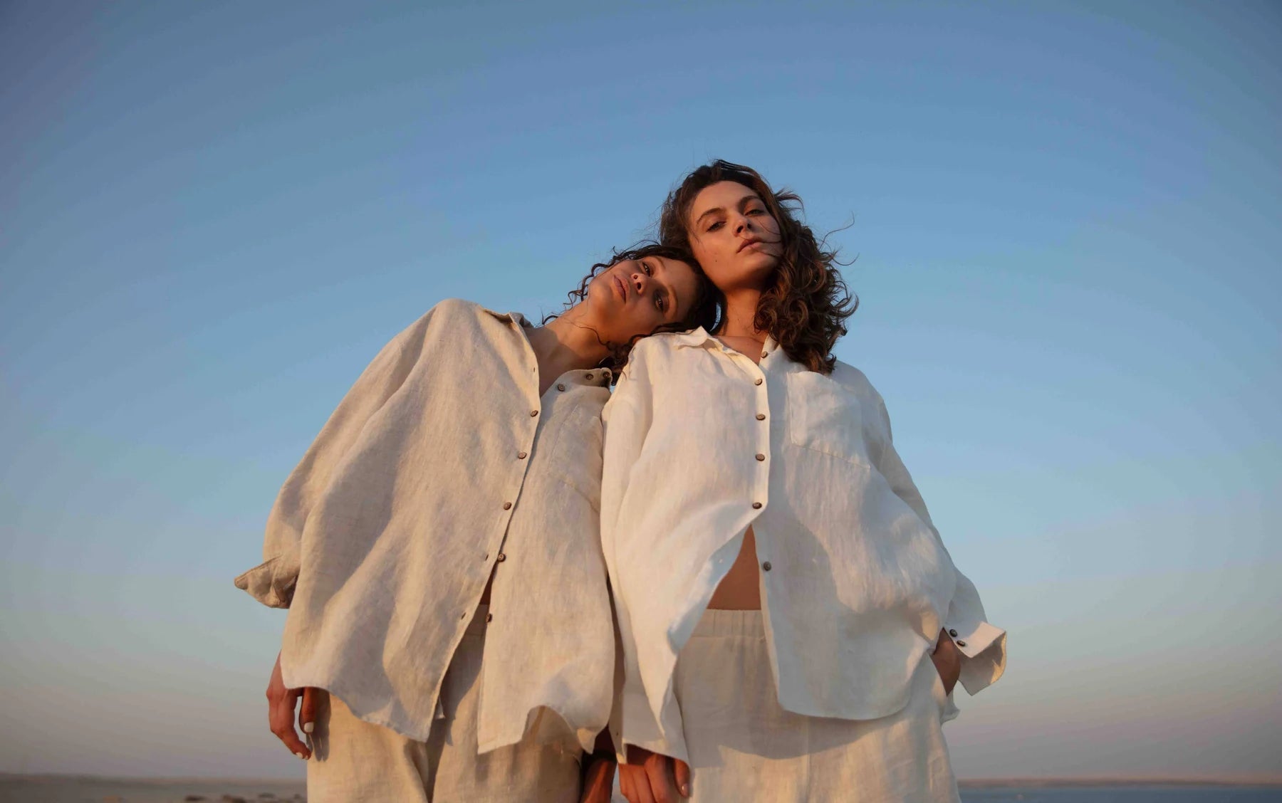 Two women in ivory linen under an open sky