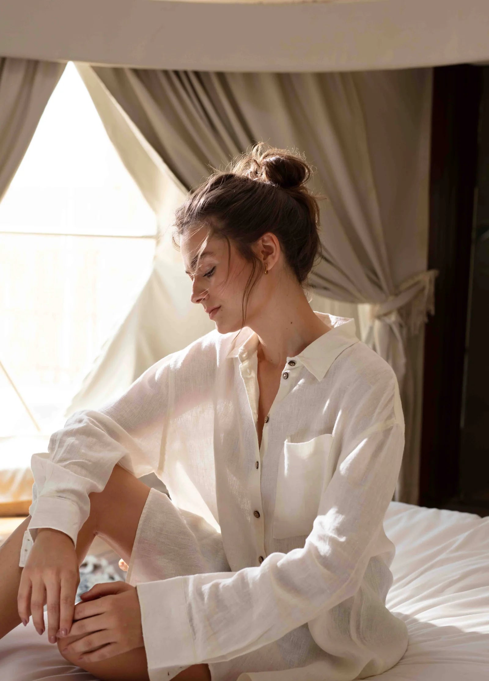 Woman wearing a white linen shirt in a softly lit room